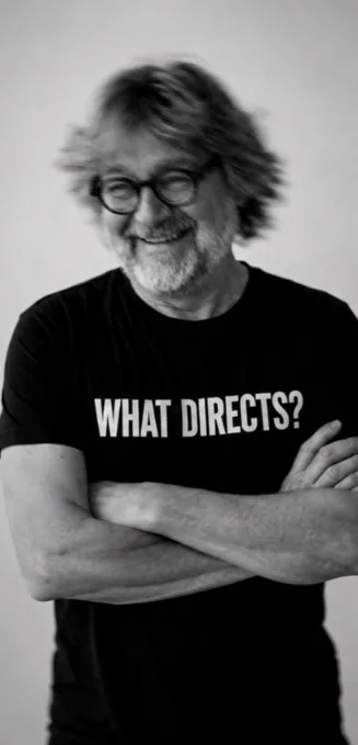 Steffen Rolla im Schwarz-Weiß-Porträt, die Arme verschränkt, schwarzes T-Shirt mit der Aufschrift WHAT DIRECTS?