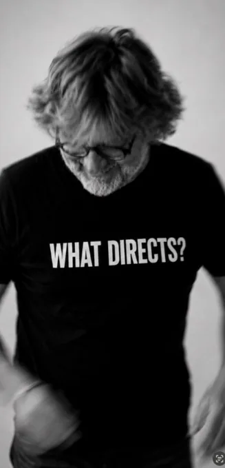 Steffen Rolla im Schwarz-Weiß-Porträt, den Blick nach unten, schwarzes T-Shirt mit der Aufschrift WHAT DIRECTS?