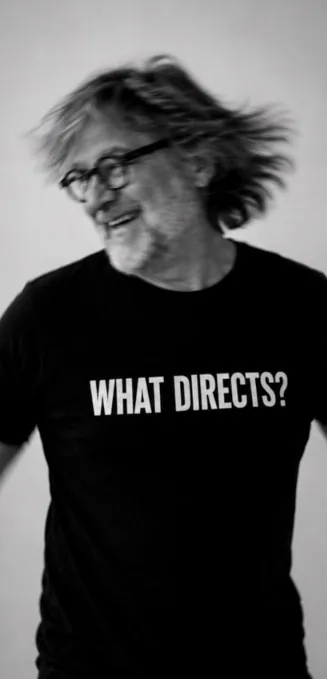 Steffen Rolla im Schwarz-Weiß-Porträt, den Kopf zur Seite gewendet, schwarzes T-Shirt mit der Aufschrift WHAT DIRECTS?
